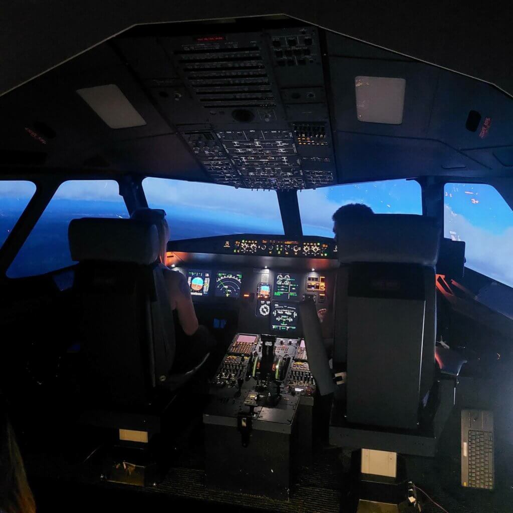 Nuoret aikuiset lentämässä Airbus A320-simulaattorilla kauniin sinisessä iltahetkessä.