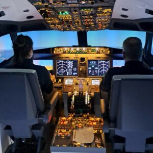 Kaksi aikuista lentämässä Boeing B737-simulaattorilla.