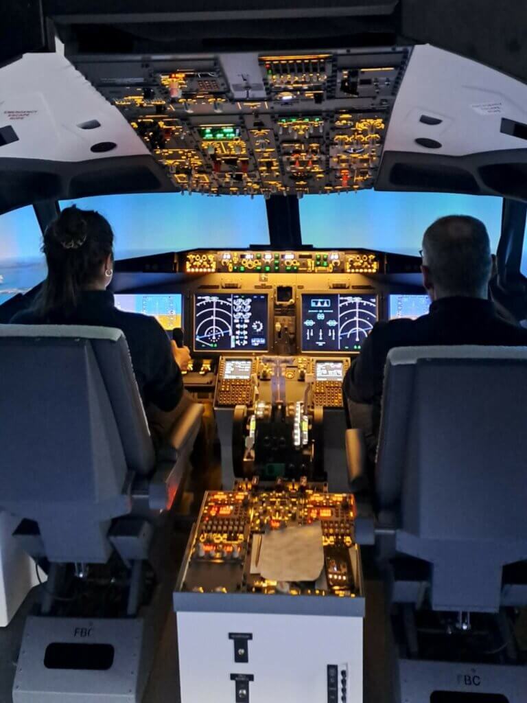 Kaksi aikuista lentämässä Boeing B737-simulaattorilla.