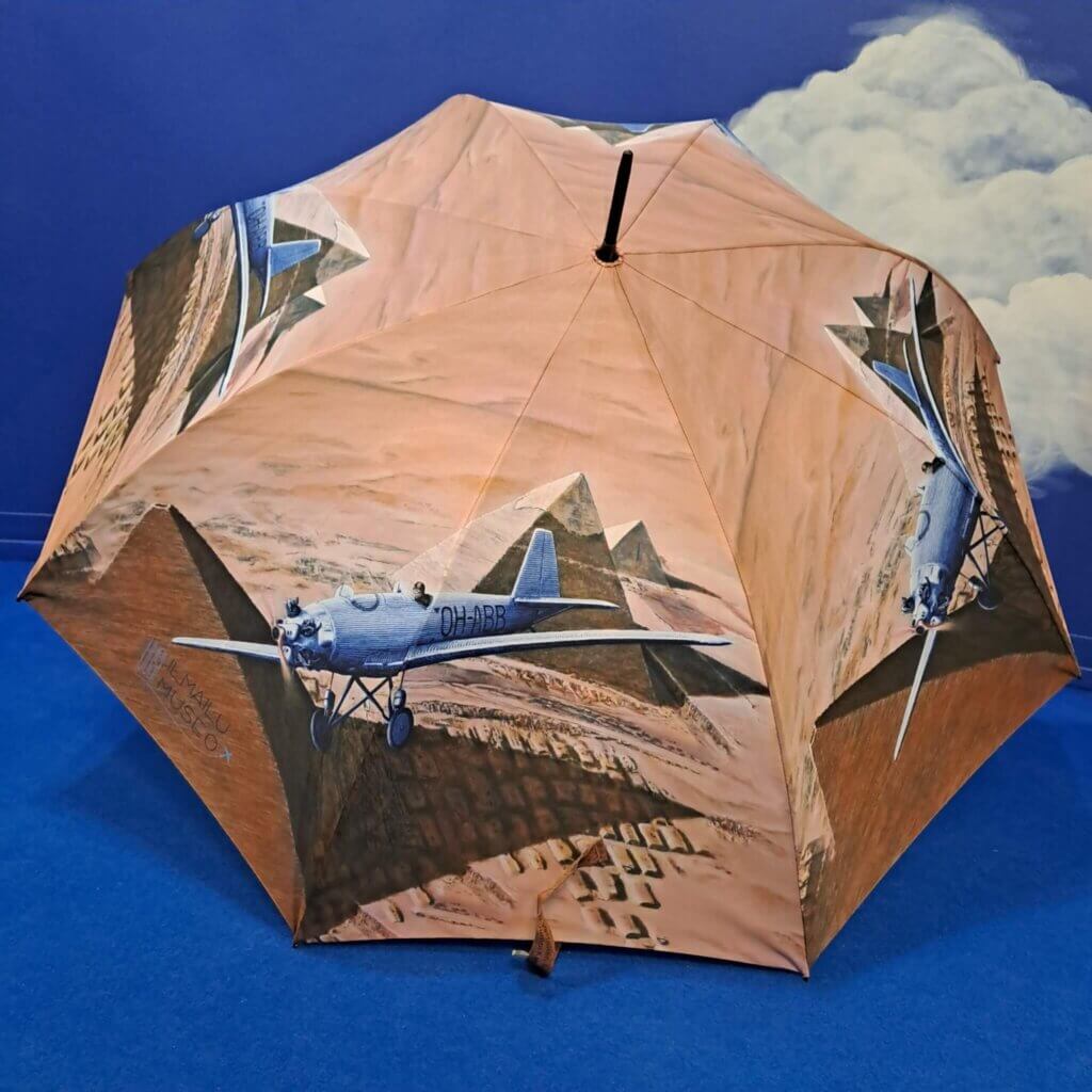 Iso sateenvarjo avattuna, varjon kuvituksena Bremerin Junkers A50 Junior lentämässä Kairon pyramidien edustalla.