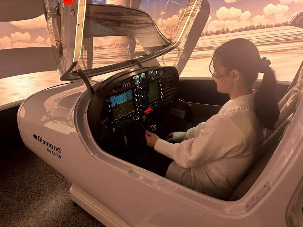 Nuori nainen iloisena Diamond DA-42 -simulaattorissa.