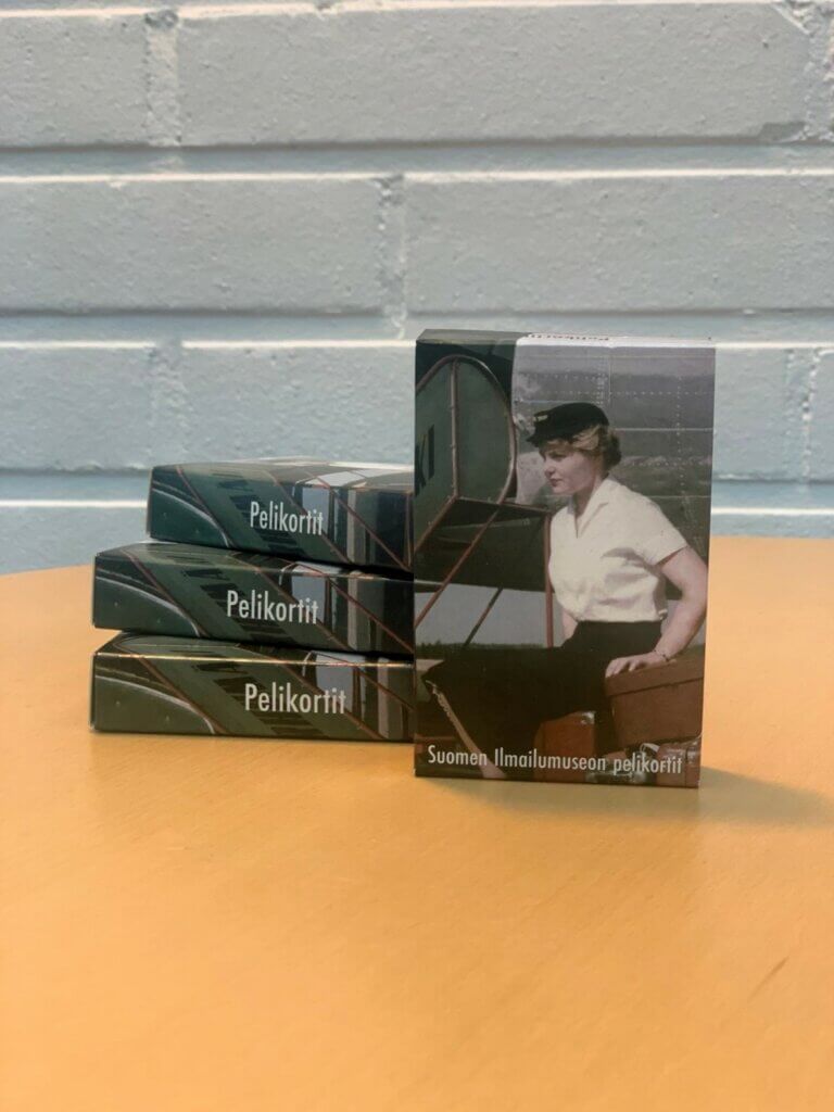 Suomen Ilmailumuseon pelikorttipakkoja pöydällä pinossa sekä yksi pystyssä kuvapuoli eteenpäin.