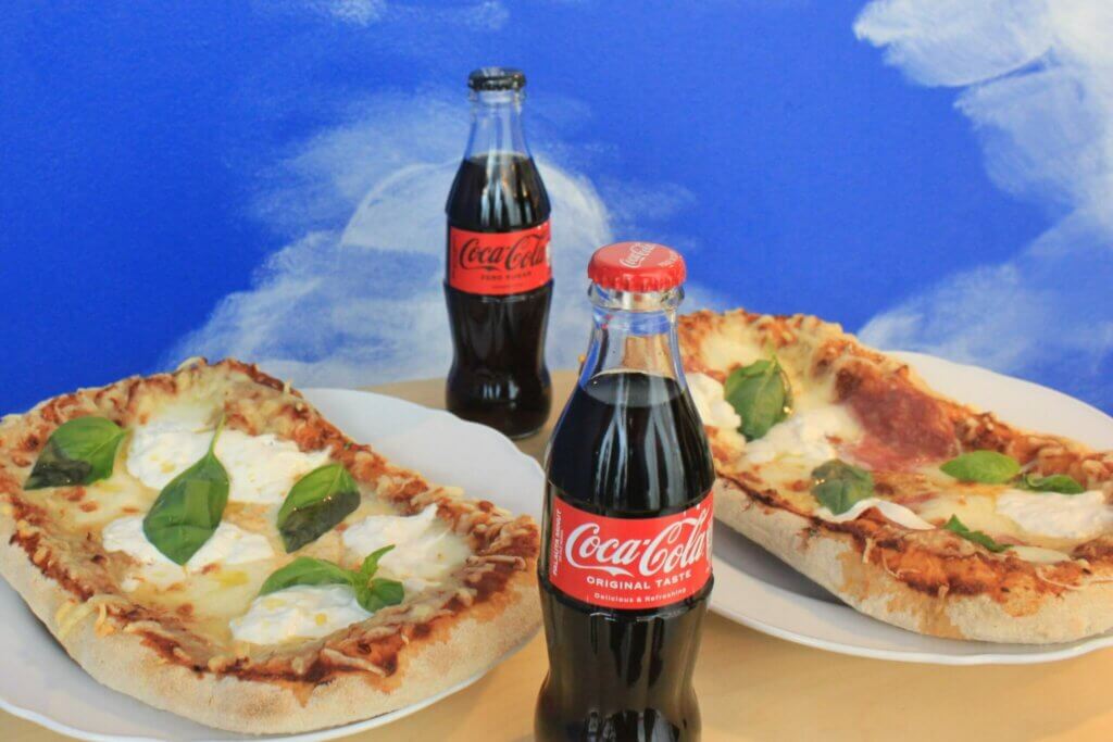 Kaksi pizzaa ja kaksi Coca-Cola-pulloa pöydällä.