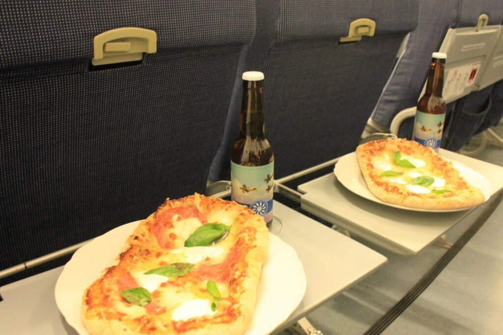 Lentokonepenkkien tarjottimilla kaksi pizzaa ja kaksi pulloa olutta.