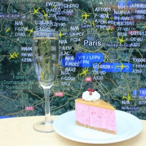 Lasillinen kuohuvaa ja pala moussekakkua pöydällä, taustalla Flight Radarin näkymä Pariisista.