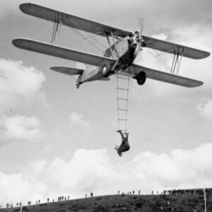 Juliste, jossa Pilvien huimapää Anneli Linna roikkuu Letov S.218 A Smolik -lentokoneen köysitikkailla.