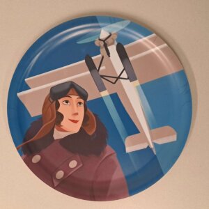 Pyöreä tarjotin, jonka kuvituksena Suomen ensimmäinen naislentäjä Vuokko Knuutila.